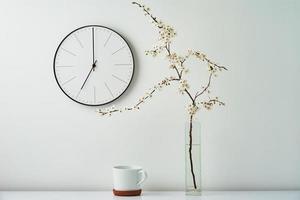 Wall clock, blooming branch and cup on white background photo