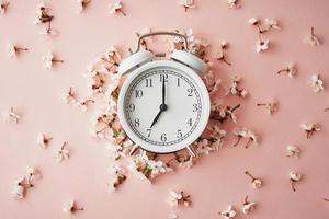 Alarm clock on pink background with flowers. Change time concept photo