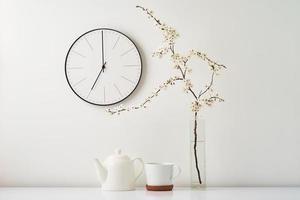 Wall clock, blooming branch and cup on white background photo