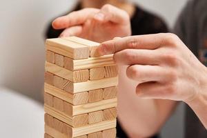 Family play board game. Hands take wooden block from tower. photo