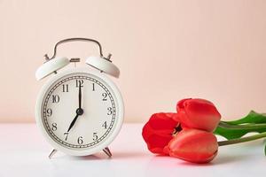 Alarm clock and flowers in vase on white background photo