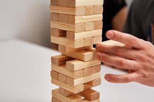 Family play board game. Hands take wooden block from tower. photo