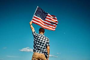 el hombre sostiene la bandera nacional de estados unidos contra el cielo azul foto