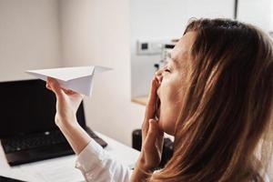 Woman plays with paper plain at home office. Procrastinate at remote work photo