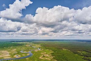 Blue cloudy sky ove river floodplain landscape and green forest, aerial view photo