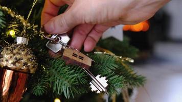 Key to the house with a keychain is hanging in hand on Christmas tree. A gift for New Year, Christmas. Building, design, project, moving to new house, mortgage, rent and purchase real estate video