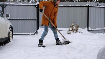 een Mens in winter reinigt sneeuw met een Schep in de werf van een huis in de parkeren kavel. sneeuwval, moeilijk weer conditie, de auto is vertragen, graven omhoog de passage video