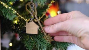 la clé de la maison avec un porte-clés est suspendue à la main sur l'arbre de noël. un cadeau pour le nouvel an, noël. construction, conception, projet, déménagement dans une nouvelle maison, hypothèque, location et achat immobilier video