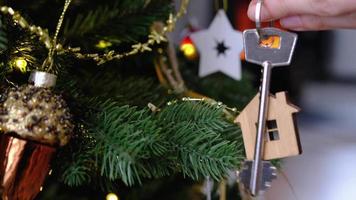 la llave de la casa con un llavero está colgada en la mano en el árbol de navidad. un regalo para año nuevo, navidad. construcción, diseño, proyecto, mudanza a casa nueva, hipoteca, alquiler y compra de bienes inmuebles video