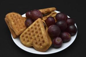 deliciosos gofres y uvas en un plato. un desayuno dulce de gofres y uvas rojas. gofres en forma de corazón. foto