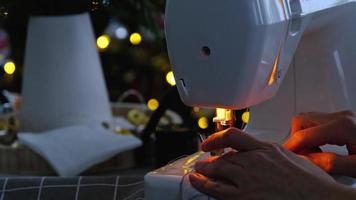 proceso de costura en una máquina de coser, una aguja con hilo y un soporte cosen de cerca la tela a cuadros blanca. preparación para navidad y año nuevo, textiles acogedores en un interior festivo video