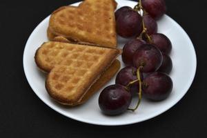deliciosos gofres y uvas en un plato. un desayuno dulce de gofres y uvas rojas. gofres en forma de corazón. foto