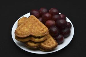 deliciosos gofres y uvas en un plato. un desayuno dulce de gofres y uvas rojas. gofres en forma de corazón. foto