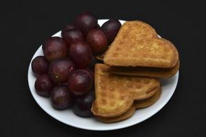 Delicious waffles and grapes on a plate. A sweet breakfast of waffles and red grapes. Heart-shaped waffles. photo