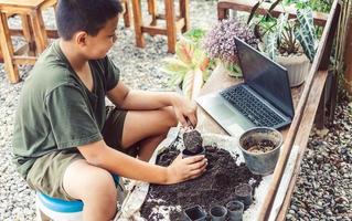 Boy learns to grow flowers in pots through online teaching. shoveling soil into pots to prepare plants for planting leisure activities concept photo