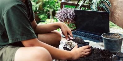 Boy learns to grow flowers in pots through online teaching. shoveling soil into pots to prepare plants for planting leisure activities concept photo