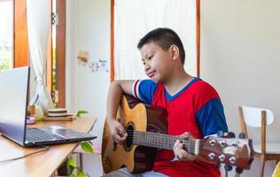 The story of a boy watching a notebook computer while preparing to practice playing guitar at home. Boys take classical guitar lessons online. photo