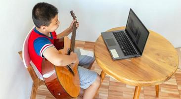 The story of a boy watching a notebook computer while preparing to practice playing guitar at home. Boys take classical guitar lessons online. photo