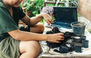 Boy learns to grow flowers in pots through online teaching. shoveling soil into pots to prepare plants for planting leisure activities concept photo