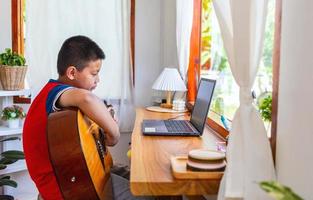 The story of a boy watching a notebook computer while preparing to practice playing guitar at home. Boys take classical guitar lessons online. photo