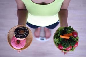 las mujeres están pesando con la balanza, sosteniendo donuts y ensaladas. la decisión de elegir comida chatarra que no es buena para la salud y vegetal rica en vitaminas es beneficiosa para el organismo. foto