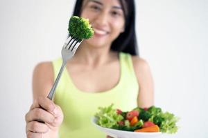 una mujer asiática feliz con un plato de ensalada saludable, sosteniendo un tenedor con un brócoli grande. alimentos para una buena forma foto
