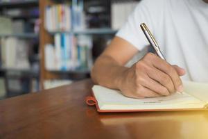 los estudiantes se sientan en la biblioteca. sostener un bolígrafo es escribir en un cuaderno. foto