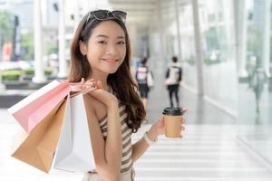 Modern happy asian Female lifestyle fashion portrait. beautiful attractive young woman girl enjoy stylish walk with shopping bag packages use smartphone on the street, trendy outfit on shopping mall photo
