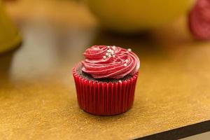 Delicious chocolate cupcake with red cream icing and sprinkles. photo