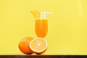 jugo de naranja vaso de verano con un trozo de fruta naranja con fondo amarillo foto