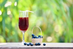 Blueberry smoothie juice glass and fresh blueberries fruit in basket with nature green summer background photo