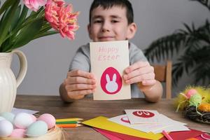 Happy boy making Easter greeting card. Materials for art creativity on kid table, children painting. Paper crafts activity in kindergarten or learning at home photo