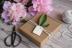 etiqueta simulada, caja de regalo kraft decorada con peonías de flores. preparación de regalos para el día de la madre, cumpleaños, fiesta de la mujer. idea para envolver regalos foto