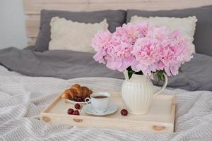 desayuno en la cama. bandeja con café, croissants y un ramo de peonías en la cama del dormitorio foto