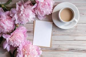 Mock up blank white paper card for text and delicate peonies on a wooden background. Flat lay, top view. Place for text. Greeting card photo