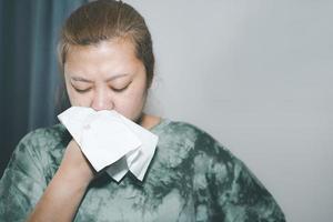 Sick woman sneezing and wiping nose with tissue in living room,feeling unhealthy and ill,There is a lot of dust. Allergies.Health care person on virus seasonal. photo