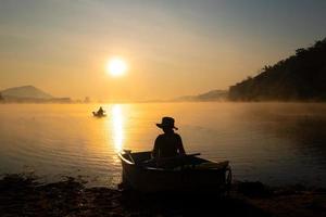 Women mooring a boat to the shore at the reservoir during the sunrise, Harirak forest park Huai Nam Man reservoir Loei Thailand 21 Jan 2023 photo