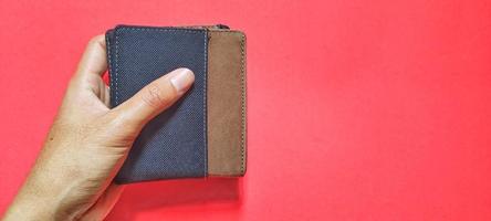 hombre sosteniendo una billetera marrón aislada en un fondo rojo. espacio negativo foto