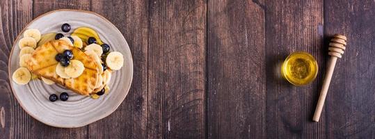 A stack of waffles with banana, blueberries and honey on a plate. Comfort food. Top view. Web banner photo