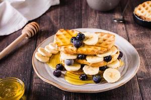 A stack of waffles with banana, blueberries and honey on a plate. Comfort food. photo