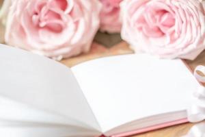 Gentle pale pink roses and open white empty blank notepad close up. Festive blur image for text. photo