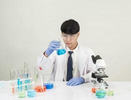 estudiante científico asiático en un laboratorio de mezcla de reactivos en un laboratorio de investigación científica con tubos de ensayo de varios tamaños y microscopios. sobre la mesa en el fondo blanco de laboratorio de química de laboratorio. foto