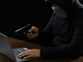 Hacker spy man one person in black hoodie sitting on a table looking computer laptop used login password attack security to circulate data digital in internet network system, night dark background. photo