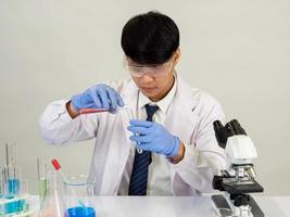 estudiante científico asiático en un laboratorio de mezcla de reactivos en un laboratorio de investigación científica con tubos de ensayo de varios tamaños y microscopios. sobre la mesa en el fondo blanco de laboratorio de química de laboratorio. foto