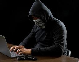 Hacker spy man one person in black hoodie sitting on a table looking computer laptop used login password attack security to circulate data digital in internet network system, night dark background. photo