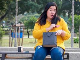 Attractive Portrait fat girl asian woman with long black hair wearing yellow T-shirt. Sitting in garden chair With a smile In hand holding the recycled paper, it is happy folded into Pink red heart photo