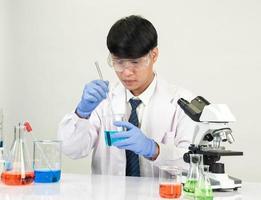 estudiante científico asiático en un laboratorio de mezcla de reactivos en un laboratorio de investigación científica con tubos de ensayo de varios tamaños y microscopios. sobre la mesa en el fondo blanco de laboratorio de química de laboratorio. foto