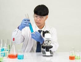 estudiante científico asiático en un laboratorio de mezcla de reactivos en un laboratorio de investigación científica con tubos de ensayo de varios tamaños y microscopios. sobre la mesa en el fondo blanco de laboratorio de química de laboratorio. foto