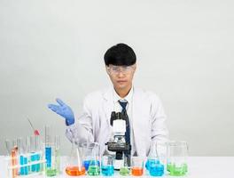 estudiante científico asiático en un laboratorio de mezcla de reactivos en un laboratorio de investigación científica con tubos de ensayo de varios tamaños y microscopios. sobre la mesa en el fondo blanco de laboratorio de química de laboratorio. foto