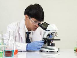 estudiante científico asiático en un laboratorio de mezcla de reactivos en un laboratorio de investigación científica con tubos de ensayo de varios tamaños y microscopios. sobre la mesa en el fondo blanco de laboratorio de química de laboratorio. foto